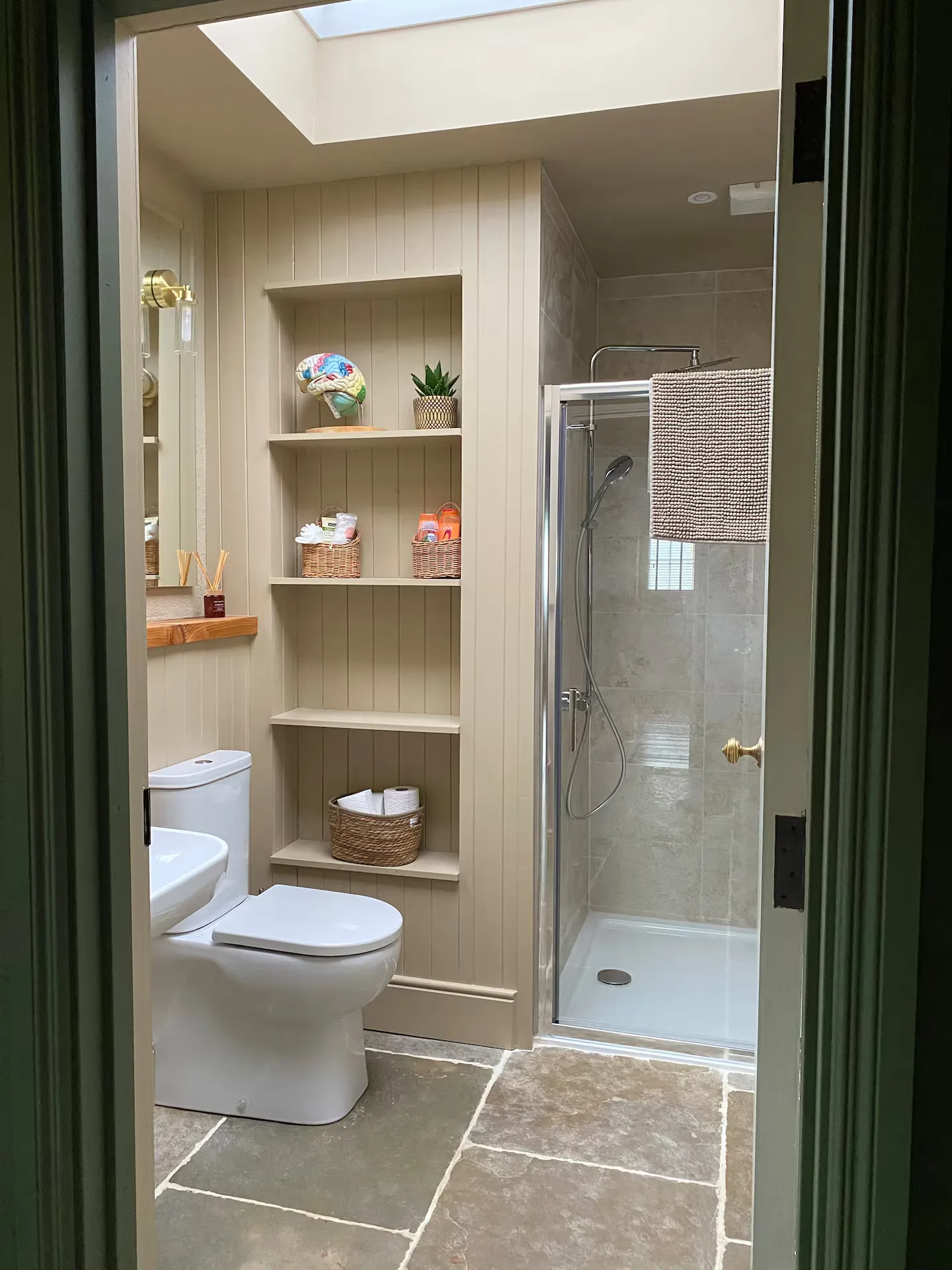 Bathroom from the doorway: beadboard panelling, built-in alcove shelving with wicker baskets, walk-in shower and skylight above
