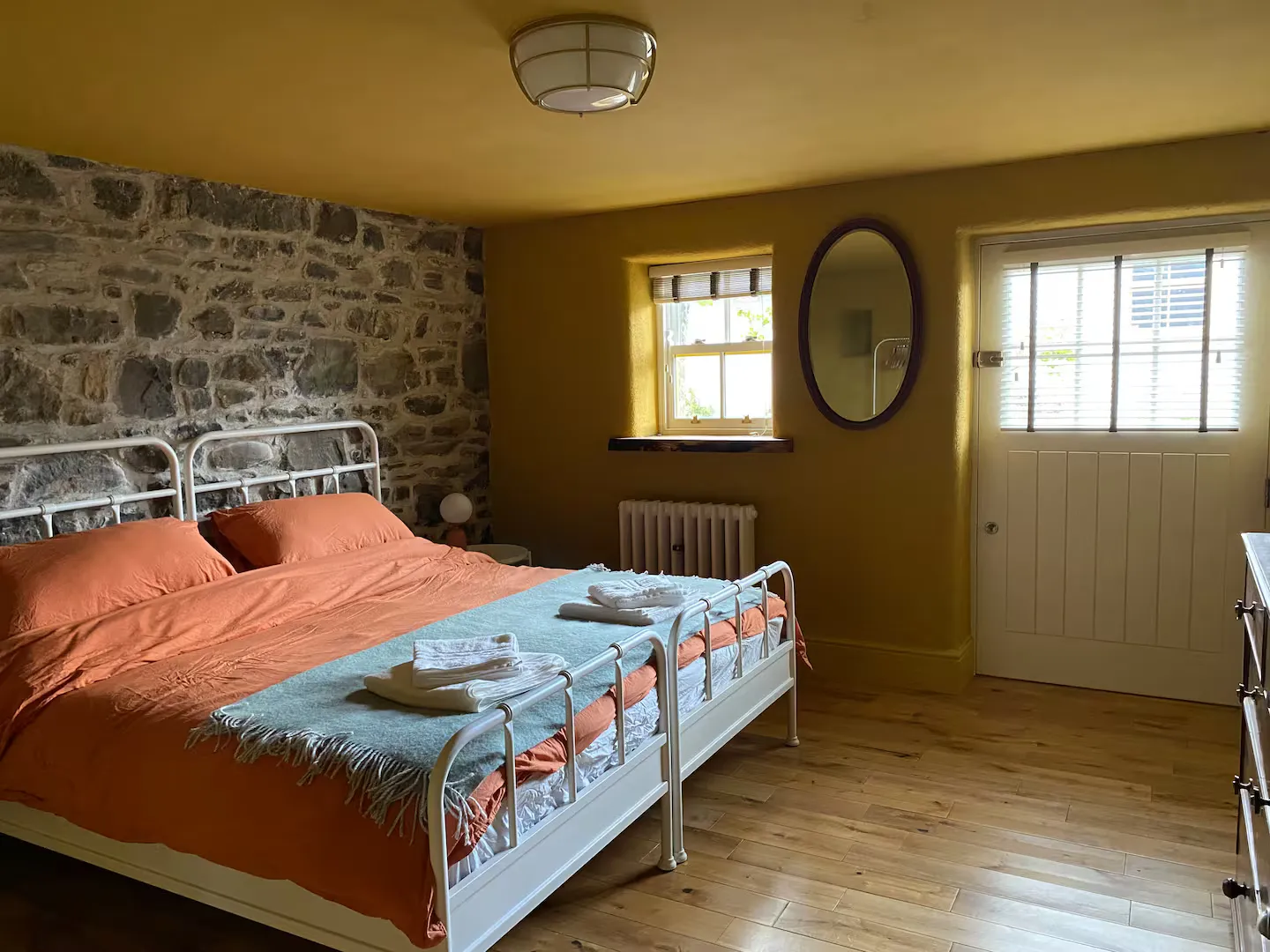 Double bedroom by day: ochre walls, exposed stone wall, oval mirror and yellow split door