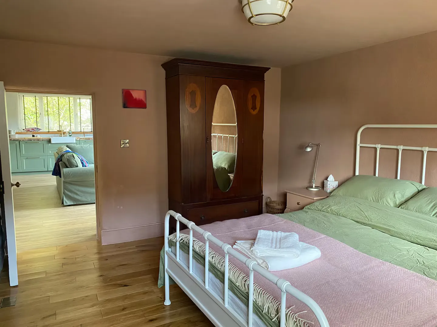 Double bedroom with dusty pink walls, large antique wardrobe with oval mirror, iron bed and green linen