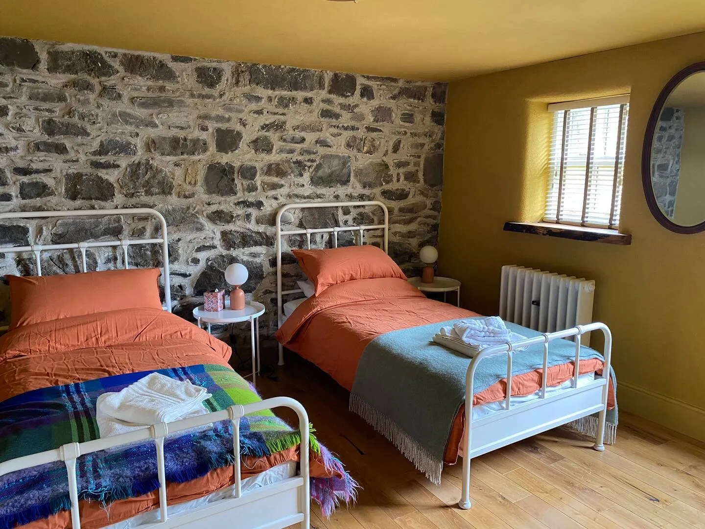 Twin bedroom with two iron beds side by side, exposed stone wall, ochre walls and terracotta linen with woven throws