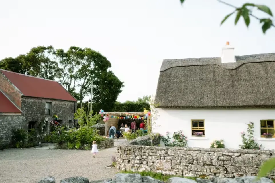 The farmyard with bunting and guests gathered, the thatched cottage and red barn roof visible