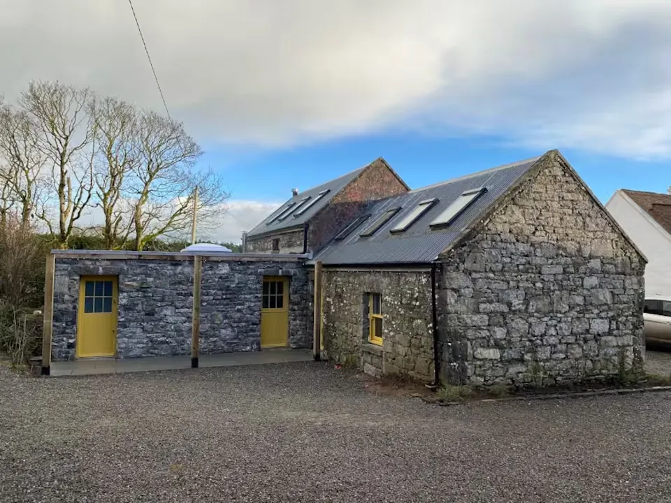 Farm outbuildings with mustard yellow doors, stone walls and a wide blue sky