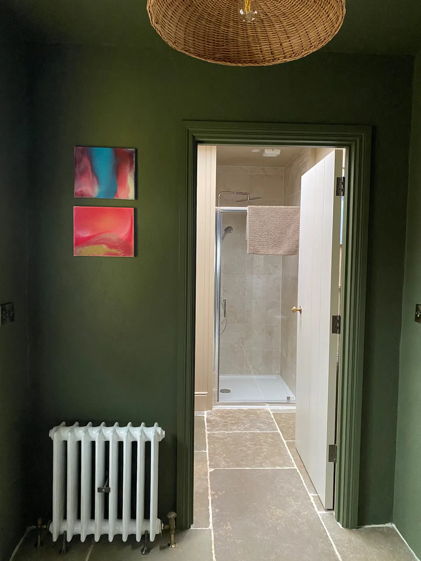 Dark green hallway with abstract artwork, wicker pendant light and view through to the bathroom beyond