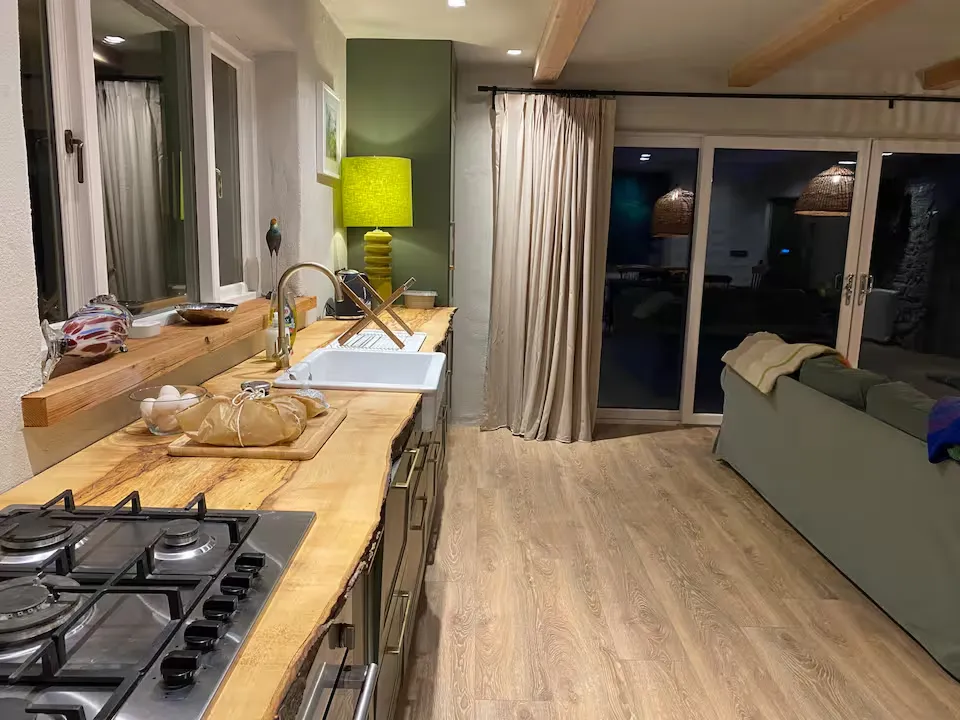 Kitchen flowing into the living room at night: warm lamp light, green cabinetry, patio doors beyond