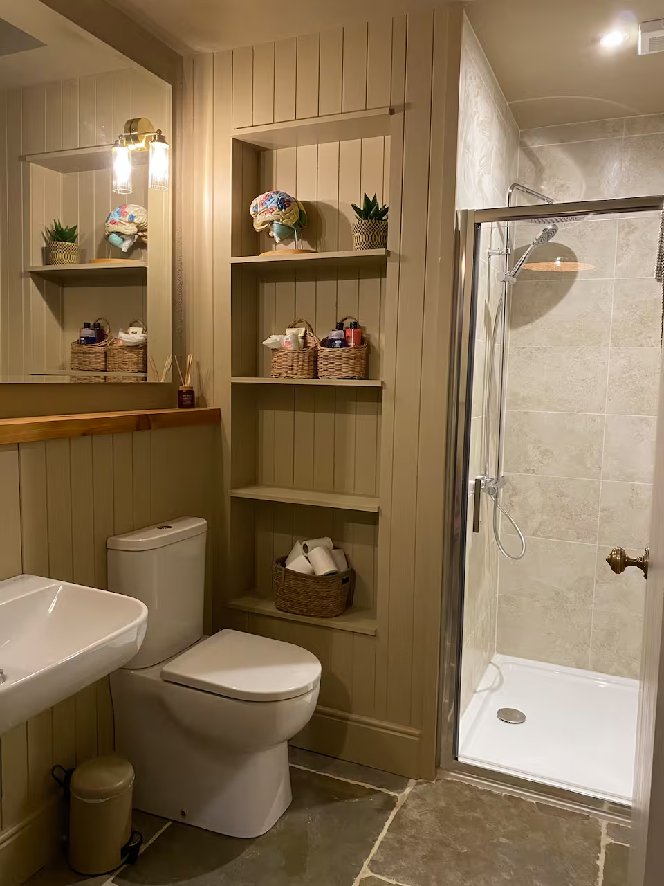 Warm bathroom with walk-in shower, built-in shelving with wicker baskets and stone tile floor