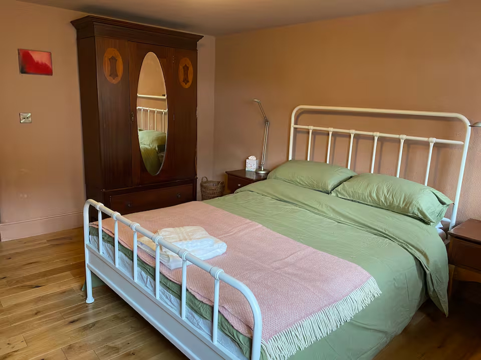 Double bedroom with antique mirrored wardrobe, iron bed frame and soft green linen