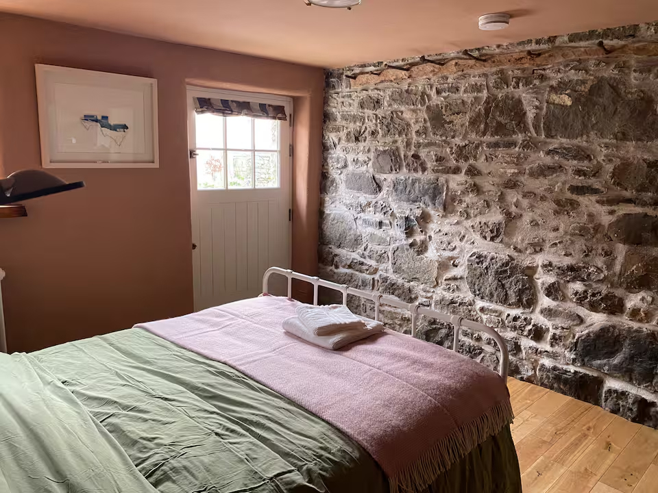 Bedroom featuring a full original stone wall, iron bed frame with pink and sage linen