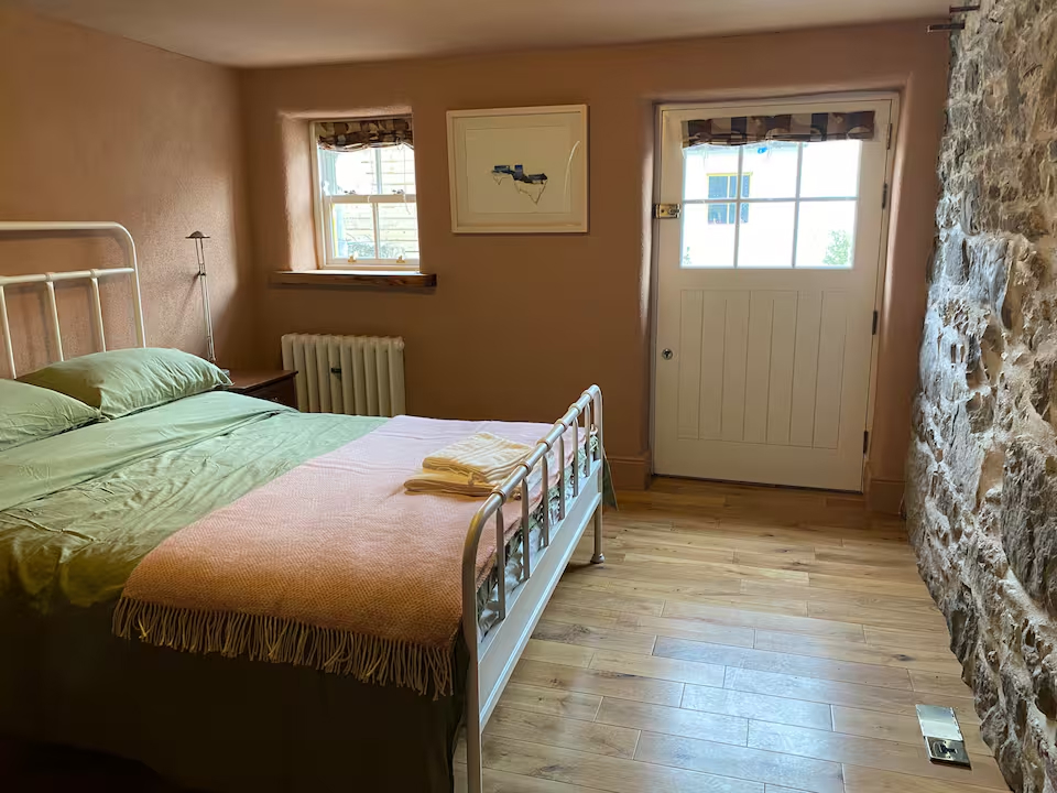 Bedroom with iron bed, exposed stone wall, small window with countryside view