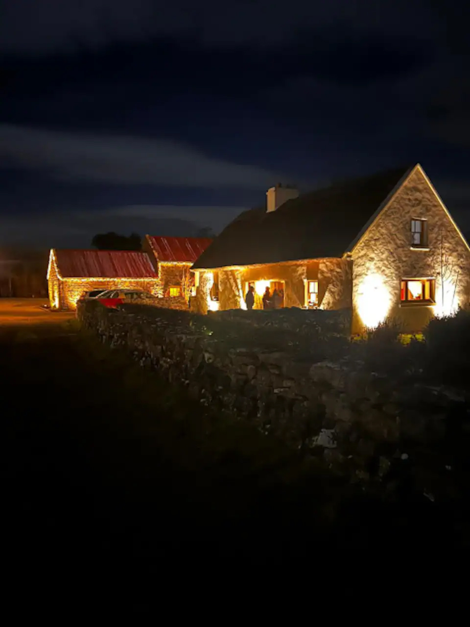 The farmhouse lit from within against a dark night sky, stone walls glowing warm