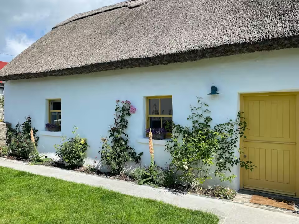 Neighbouring thatched cottage with a mustard door and climbing roses — the wider setting