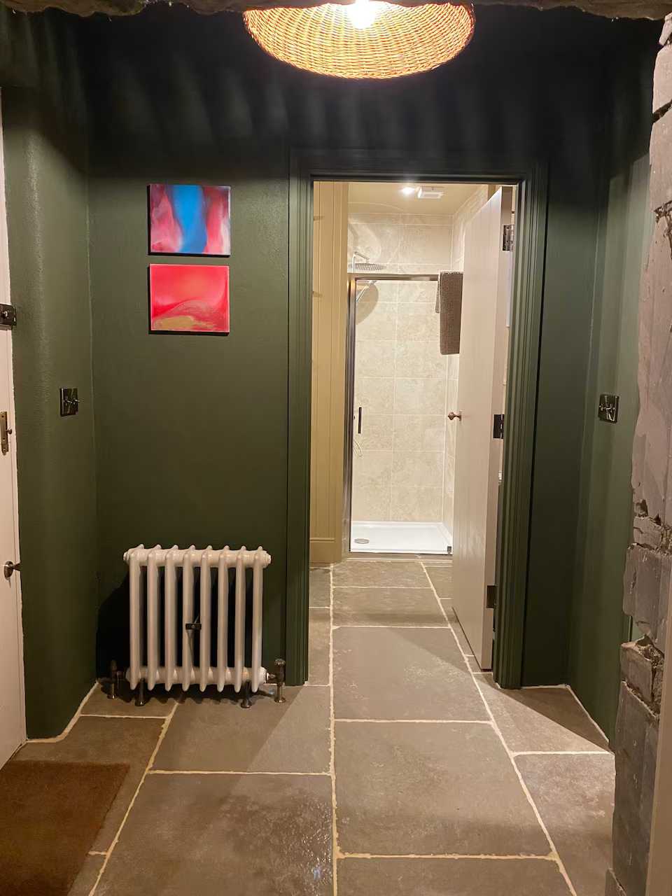 Corridor with deep green walls, flagstone floor, colourful artwork and view through to the bathroom