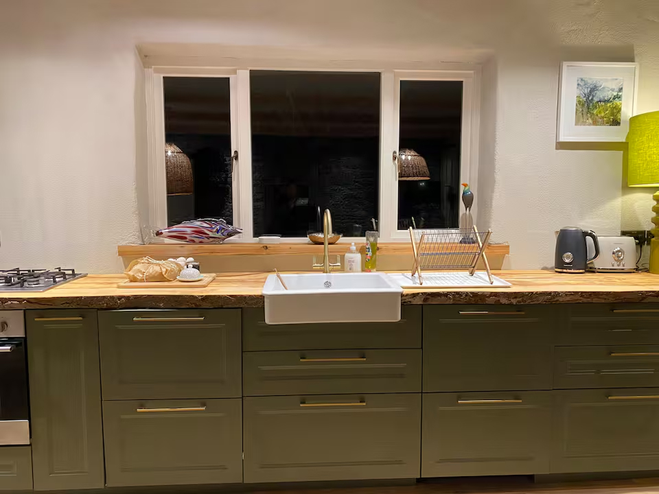 Sage green kitchen cabinets with a Belfast sink, live-edge timber worktop and triple window