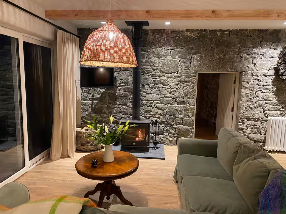 Log-burning stove with a vase of white lilies on a small round table, stone wall behind