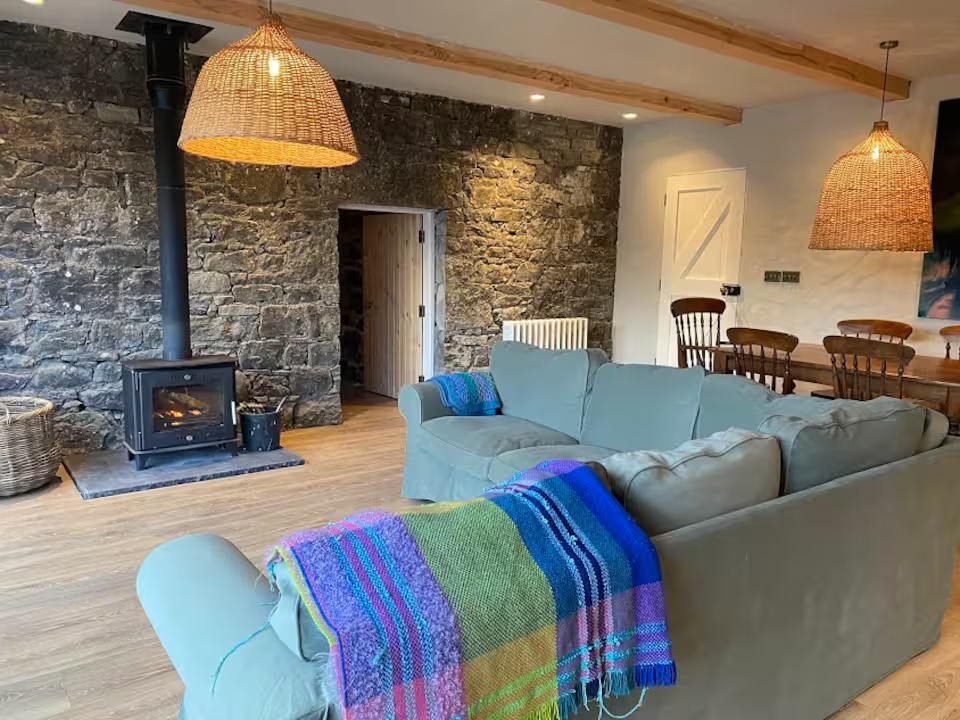 Open living room with log-burning stove, exposed stone wall, teal sofa and wicker pendant lights